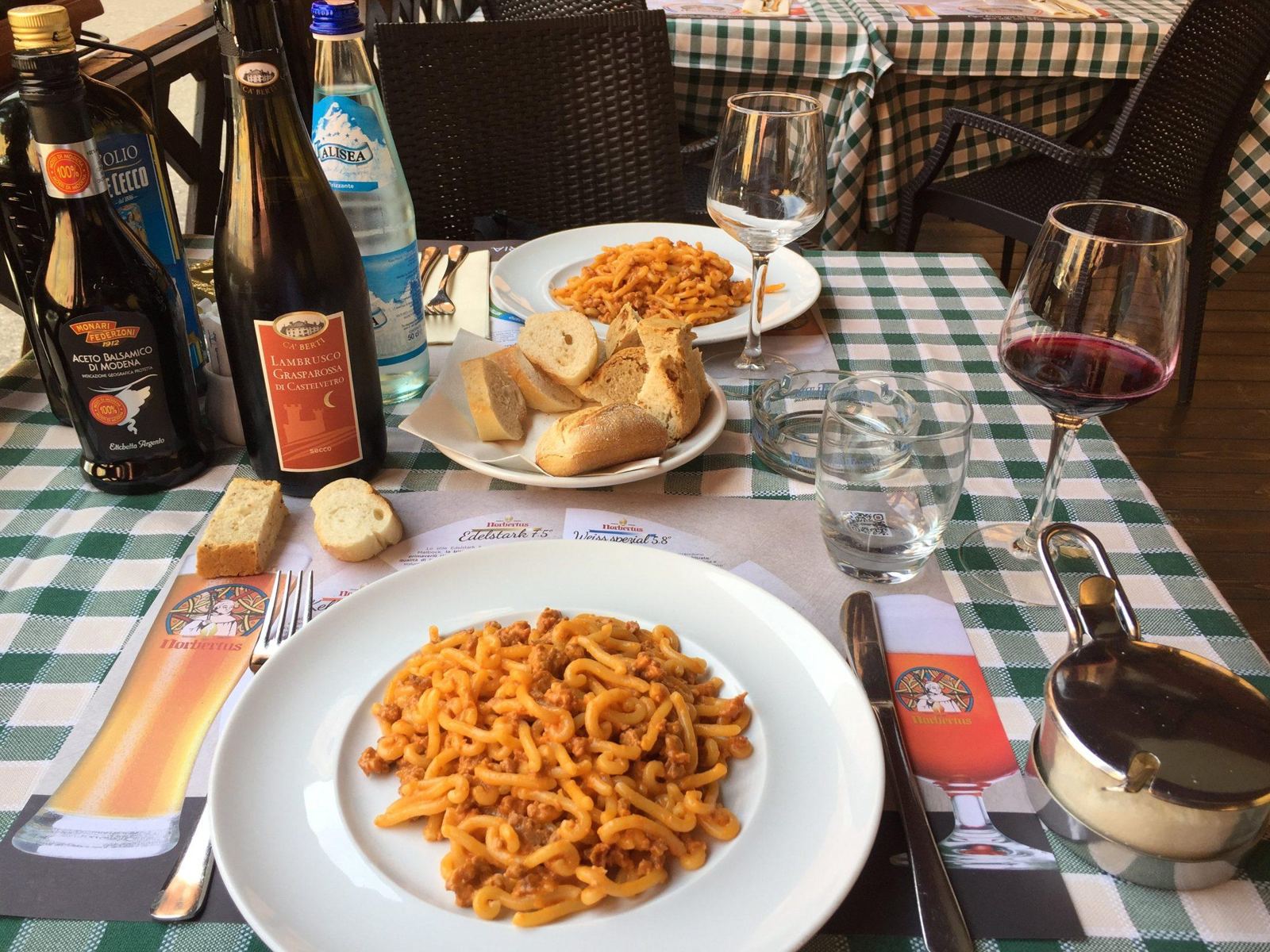 Gramigna alla salsiccia con Lambrusco, sulla tovaglia a quadretti.