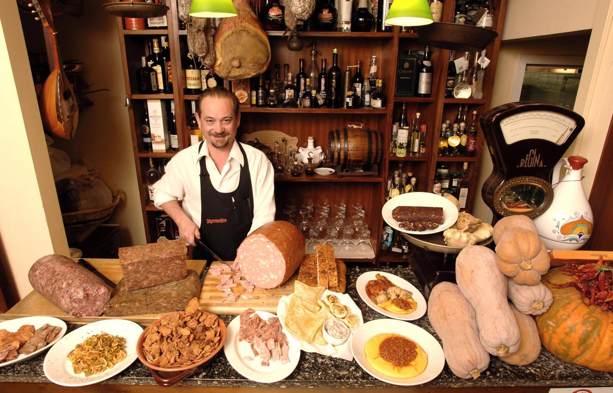 Il patron della Trattoria del Giardinetto affetta i salumi dietro il bancone, fra Lambruschi, la vecchia bilancia Regina e le zucche per i tortelli.